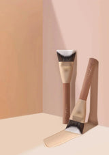 Two makeup brushes with brown handles and white bristles on a peach background