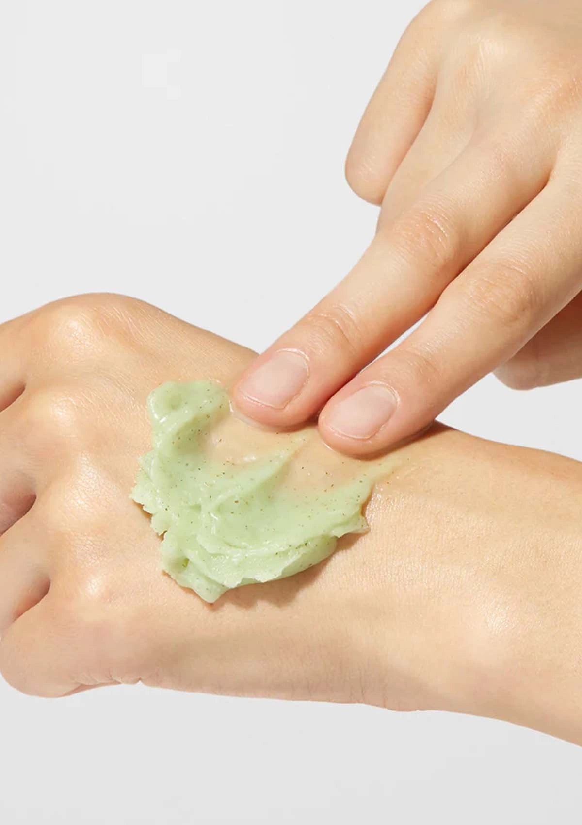Hand applying green cream to another hand on a light gray background