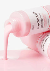 Pink bottle of Medicube toner with pink liquid being poured out on a white background