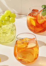 Two glasses of orange cocktails with ice and fruit on a light surface