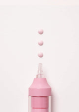 A close-up of a pink cosmetic applicator or dropper bottle with a clear tip, shown against a plain white background with three small pink droplets floating above the opening.
