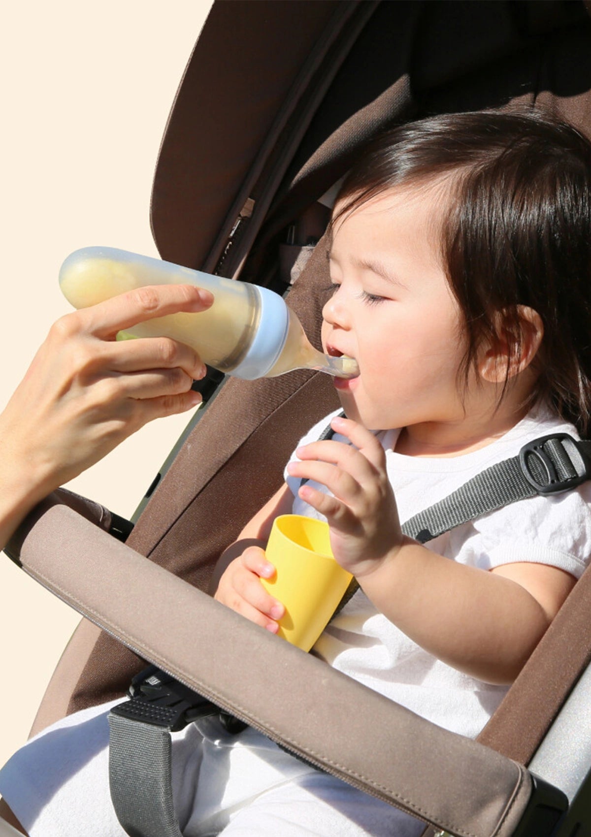 Child in a car seat being fed from a bottle by an adult