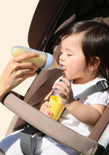 Child in a car seat being fed from a bottle by an adult