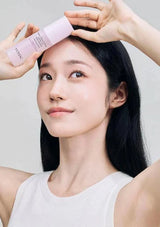 Woman applying a pink skincare product to her face with a neutral background