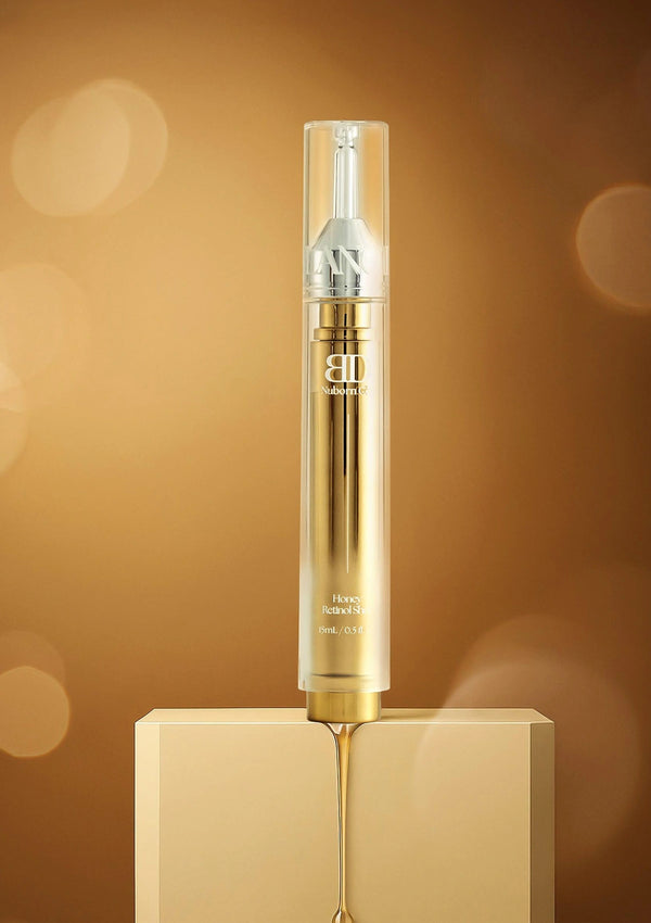 Gold and silver skincare serum bottle on a beige platform with a blurred brown background