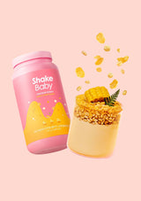 Pink 'Shake Baby' protein shake container next to a cup of dessert on a pink background