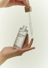 Hand holding a dropper bottle with a droplet of liquid on a plain background