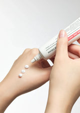 Hand applying cream from a tube to skin with visible cream dots.