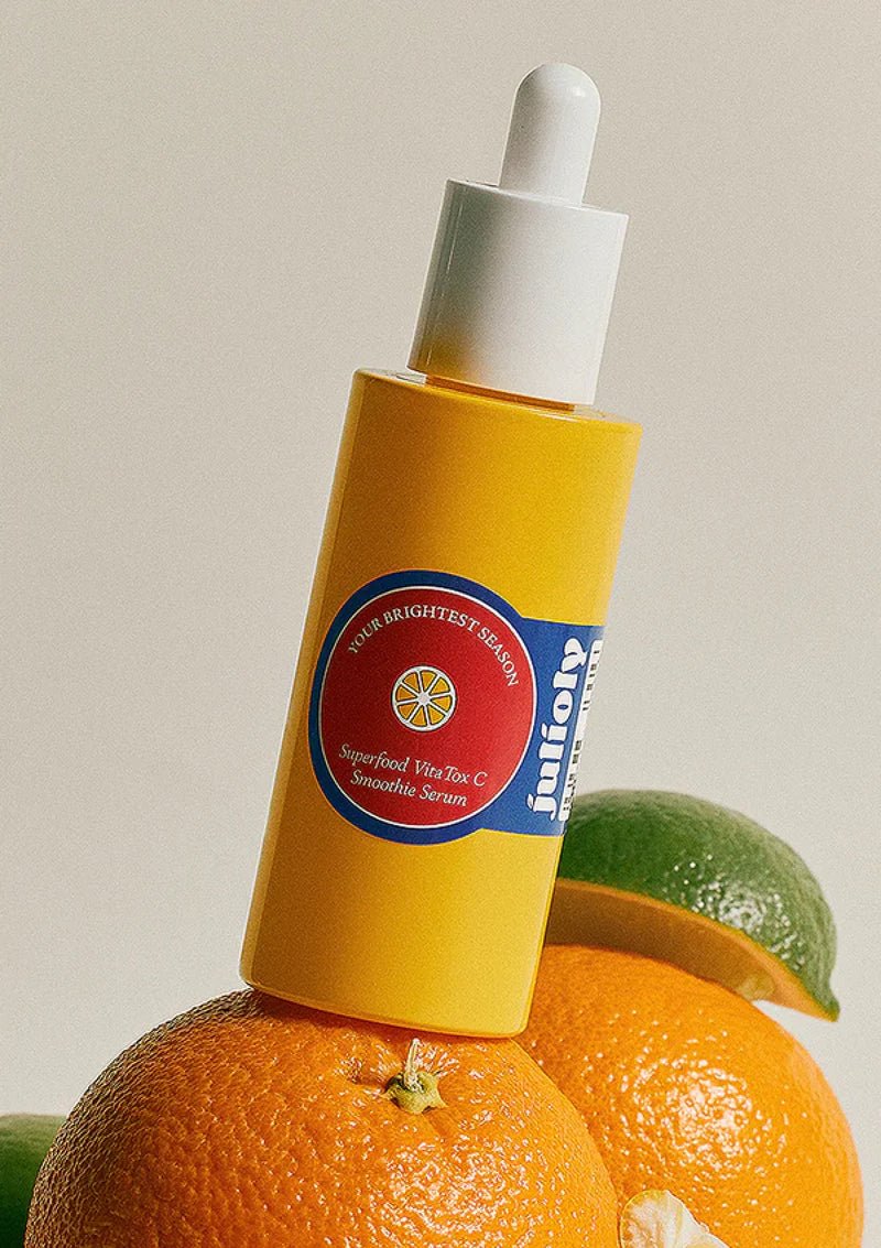Yellow bottle with a dropper on oranges and a lime against a neutral background