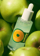 Bottle of green apple facial serum with a dropper on green apples