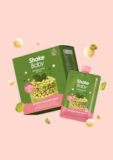Shake Baby protein powder pouch and box in green and pink packaging, floating on a soft pink background with scattered cereal pieces.