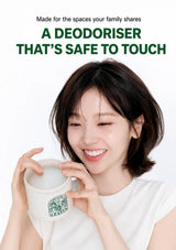 A smiling woman with short dark hair holds a white ceramic mug with a green Starbucks Plant Based Coffee logo against a clean white background. Text at the top reads, 'Made for the spaces your family shares A DEODORISER THAT'S SAFE TO TOUCH'.