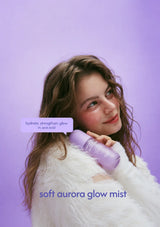 A woman with long wavy brown hair wearing a fluffy white sweater holds a lavender bottle labeled 'soft aurora glow mist' against a solid lavender background. A speech bubble reads 'hydrate, strengthen, glow, in one mist'.