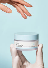 Jar of skincare cream held by a hand against a light blue background