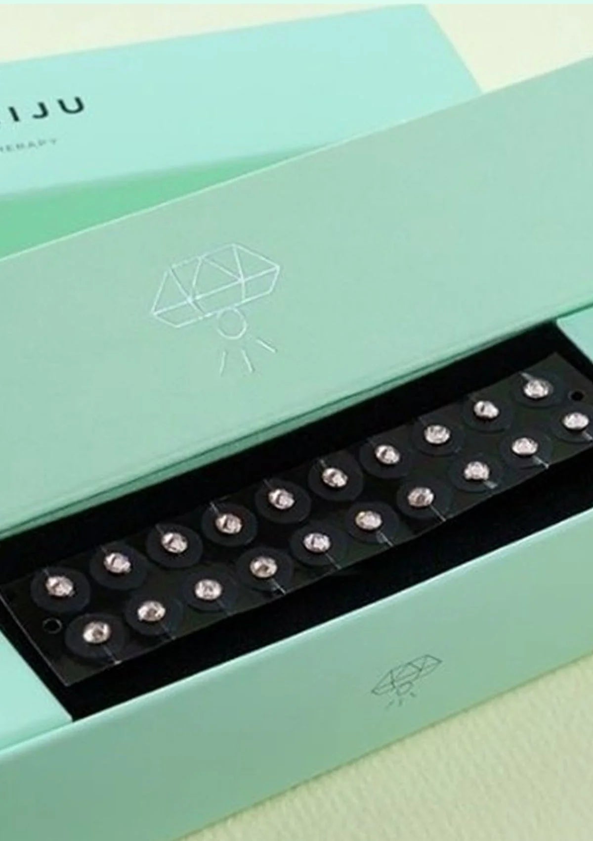 Teal box with a black tray containing small round objects on a light green background
