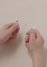 Two hands holding small metallic objects against a beige background