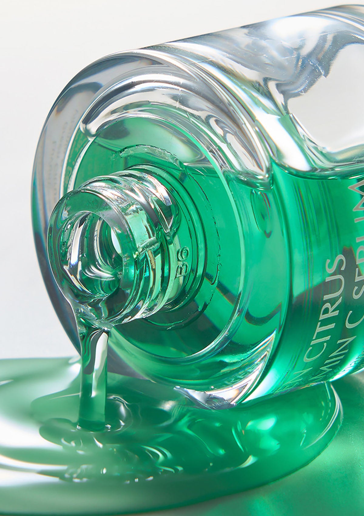 Close-up of a green bottle with liquid spilling out on a light gray background