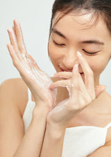 Woman applying cream to her face with a neutral background