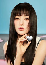 Woman holding a silver heart-shaped compact mirror against a blue background