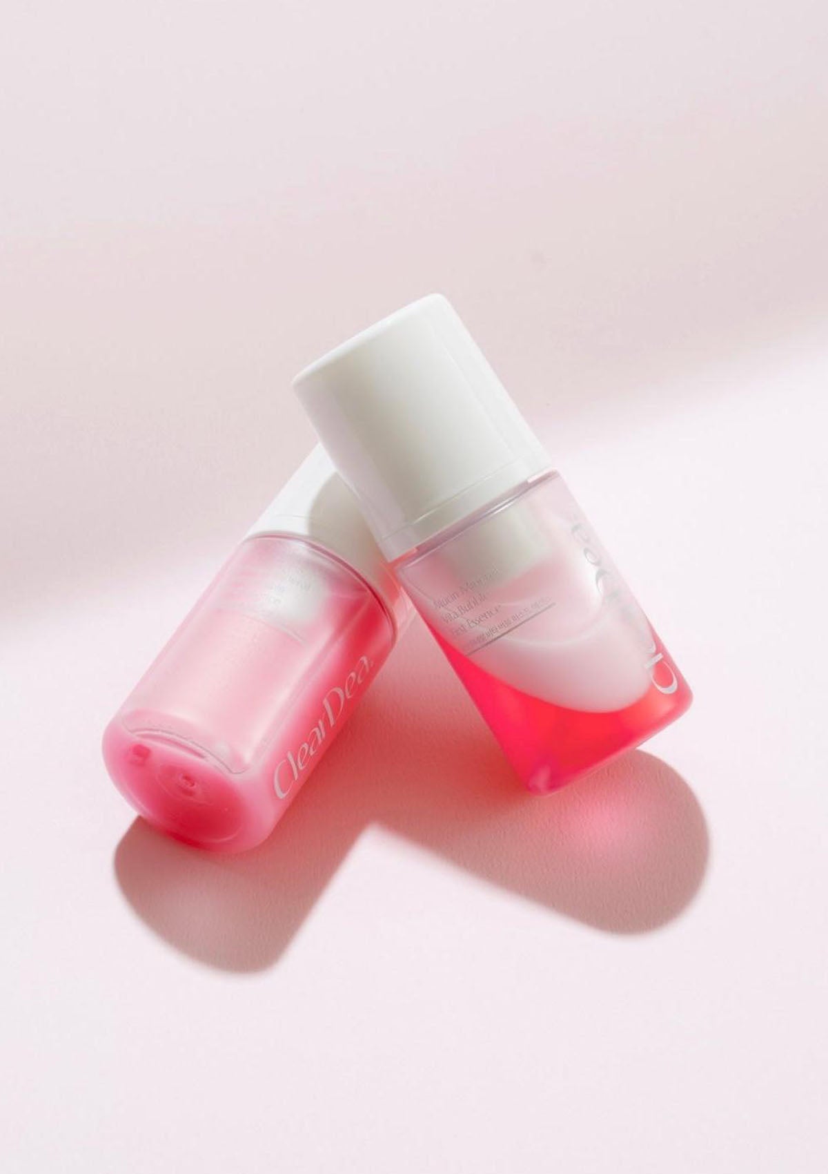Two pink bottles with white caps on a light pink background